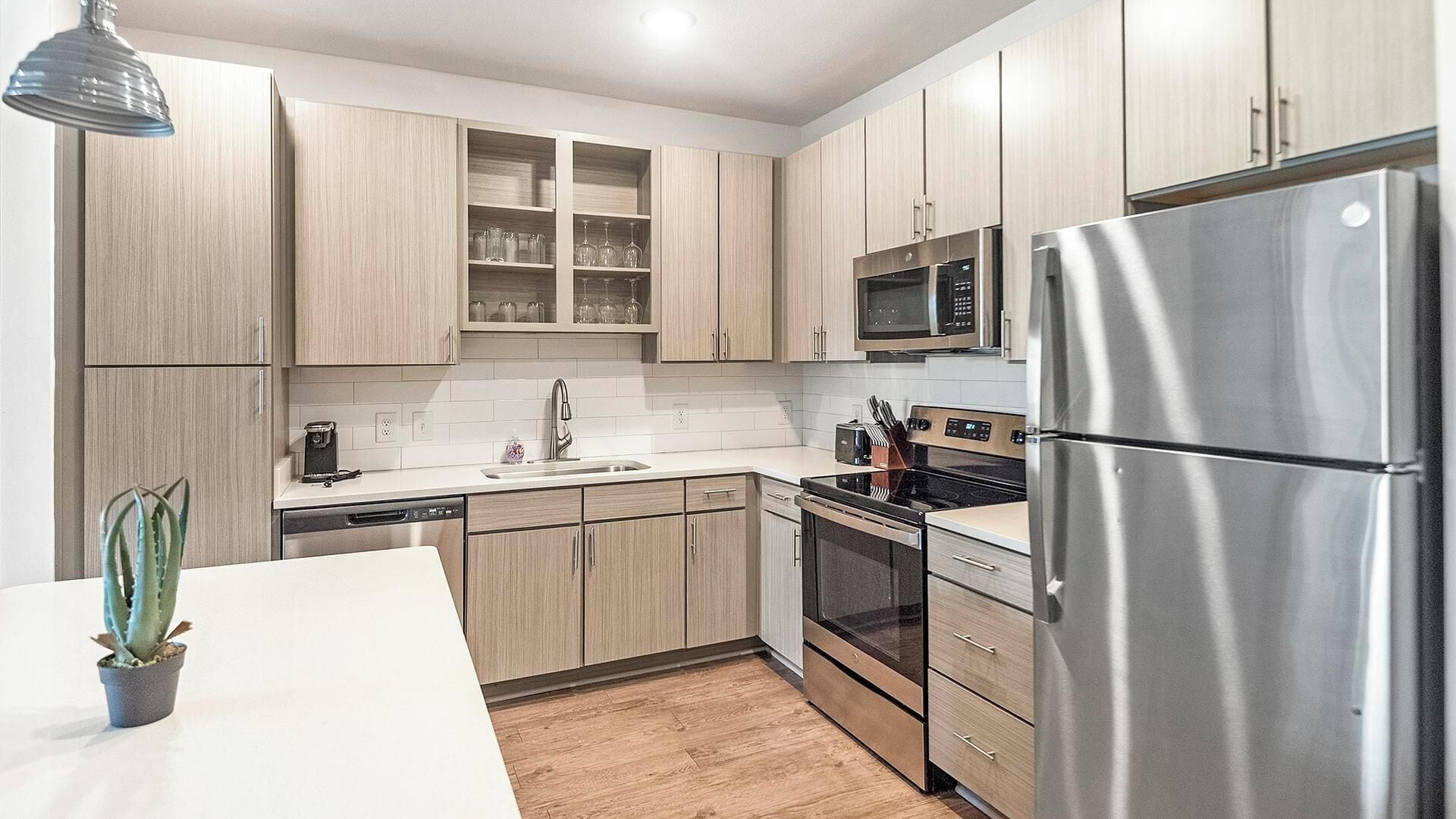 A modern kitchen with light wood cabinets, stainless steel appliances, and a white countertop.