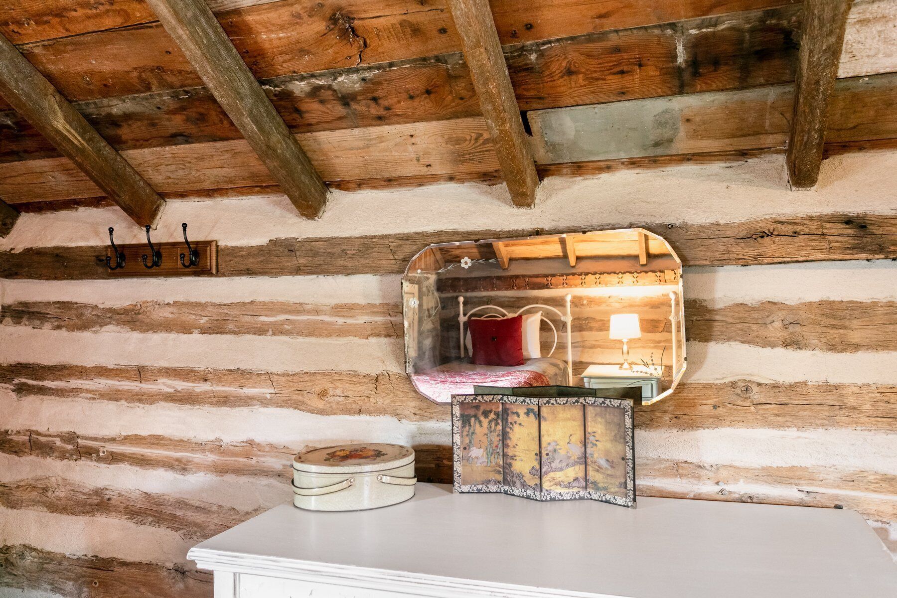 A rustic log cabin interior with a bed, a mirror, and a small table.