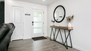 A modern entryway with a white door, a console table with a mirror, and a black leather couch. - Roadrunner Ridge | 3/3, Game Room, Hot Tub, Fire Pit & Grill, Pets w/ fee (Fredericksburg)