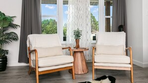 Two white armchairs with wooden frames and a round wooden table with a plant between them. - Roadrunner Ridge | 3/3, Game Room, Hot Tub, Fire Pit & Grill, Pets w/ fee (Fredericksburg)