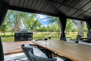 An outdoor dining area with a grill, two wine glasses, and wicker furniture. - Roadrunner Ridge | 3/3, Game Room, Hot Tub, Fire Pit & Grill, Pets w/ fee (Fredericksburg)