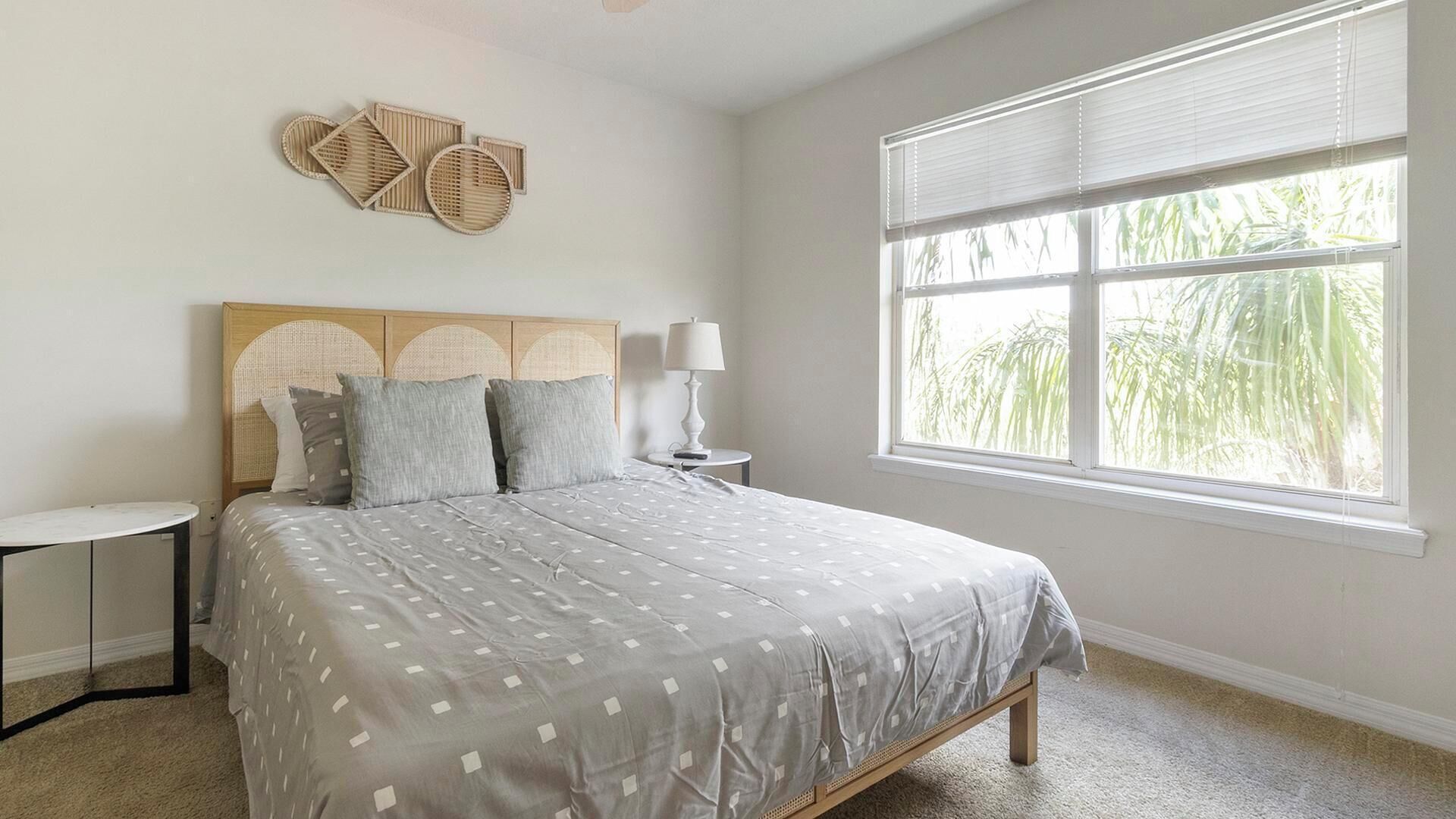 A bedroom with a bed, bedside table, lamp, and a window with blinds.