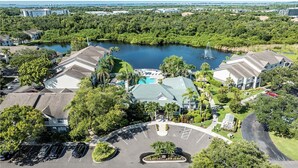 Vue aérienne d’un complexe hôtelier doté d’une piscine centrale, entouré d’une végétation luxuriante et bordé d’un lac.
