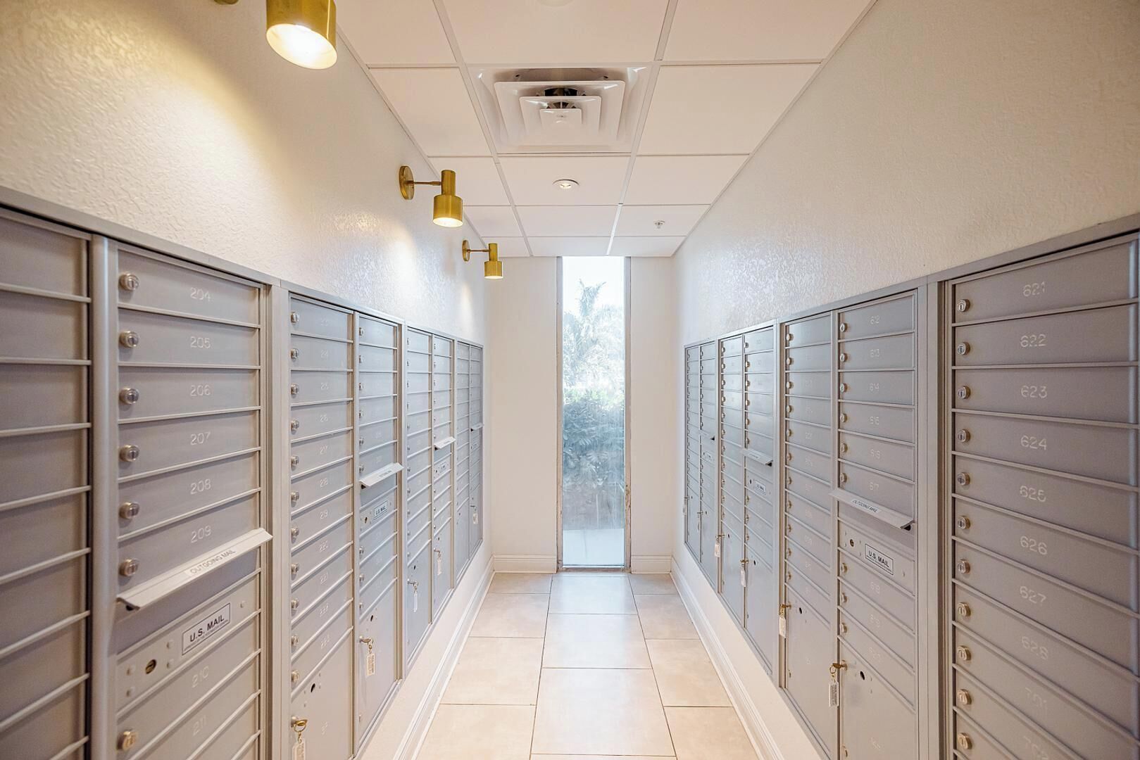 A hallway with rows of metal mailboxes numbered 200 to 210, a U.S. Mail label, and a view of trees through a window.