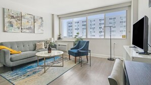 Ein modernes Wohnzimmer mit einem grauen Sofa, einem blauen Sessel, einem Couchtisch und einem großen Fenster mit Blick auf die Stadt.