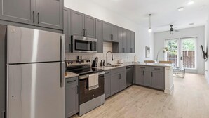 A modern kitchen with stainless steel appliances, grey cabinetry, and a wooden floor.