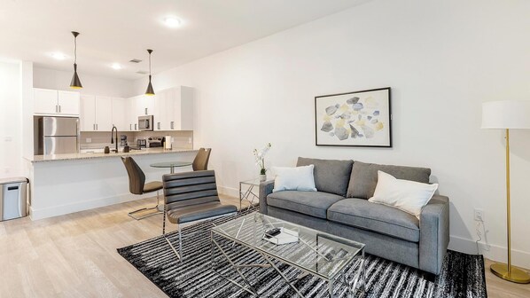 Una sala de estar moderna con un sofá gris, una mesa de centro de vidrio y una alfombra blanco y negro.