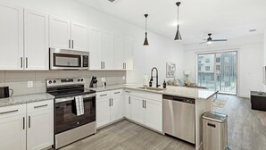 A modern kitchen with white cabinetry, stainless appliances, and a built-in dishwasher. - Landing | Stylish 1BD, Pool, Gym (Denton)