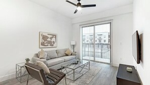 A living room with a sofa, armchair, coffee table, and a TV on a stand. - Landing | Stylish 1BD, Pool, Gym (Denton)