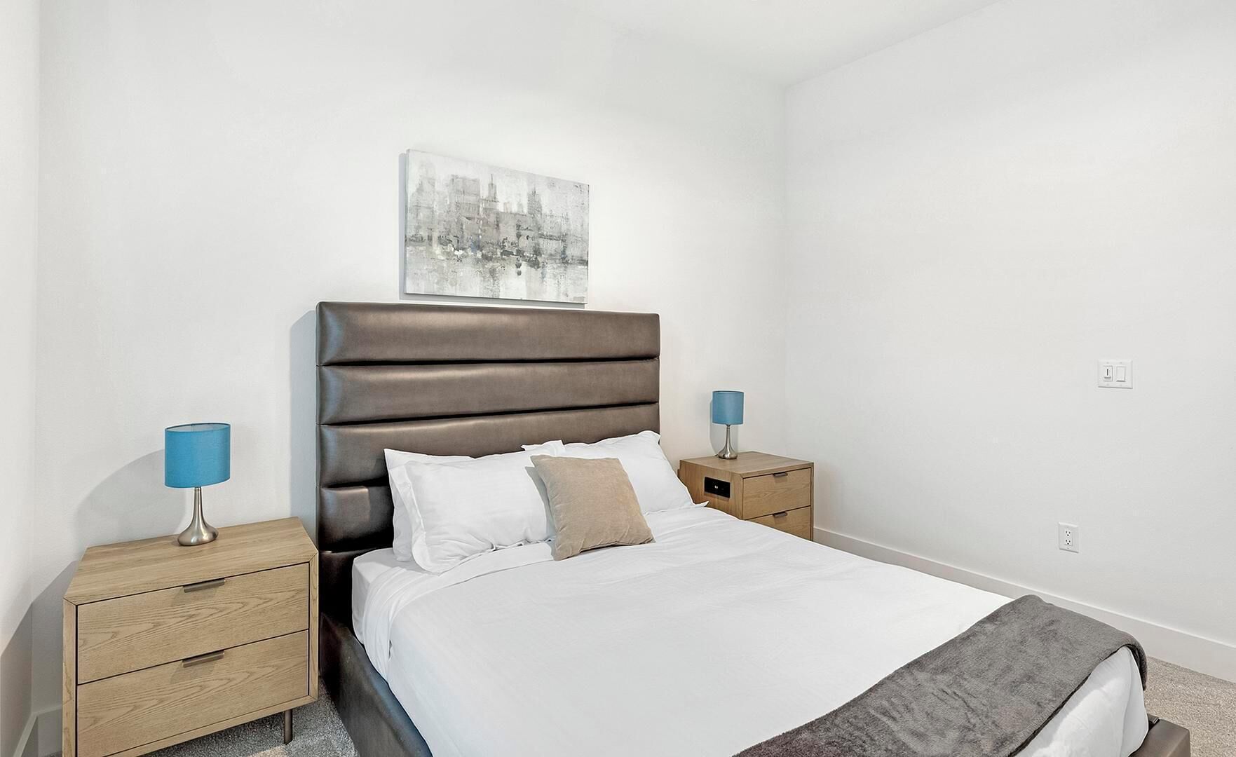 A bedroom with a bed, two bedside tables, a headboard, and a wall-mounted artwork.
