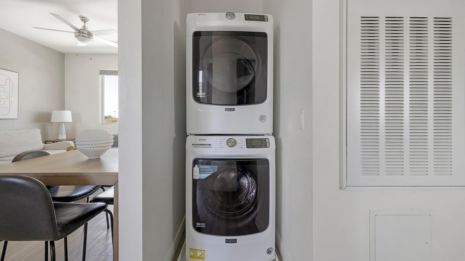 Une buanderie équipée de deux machines à laver Maytag superposées, d’un ventilateur de plafond et d’une fenêtre avec des stores.