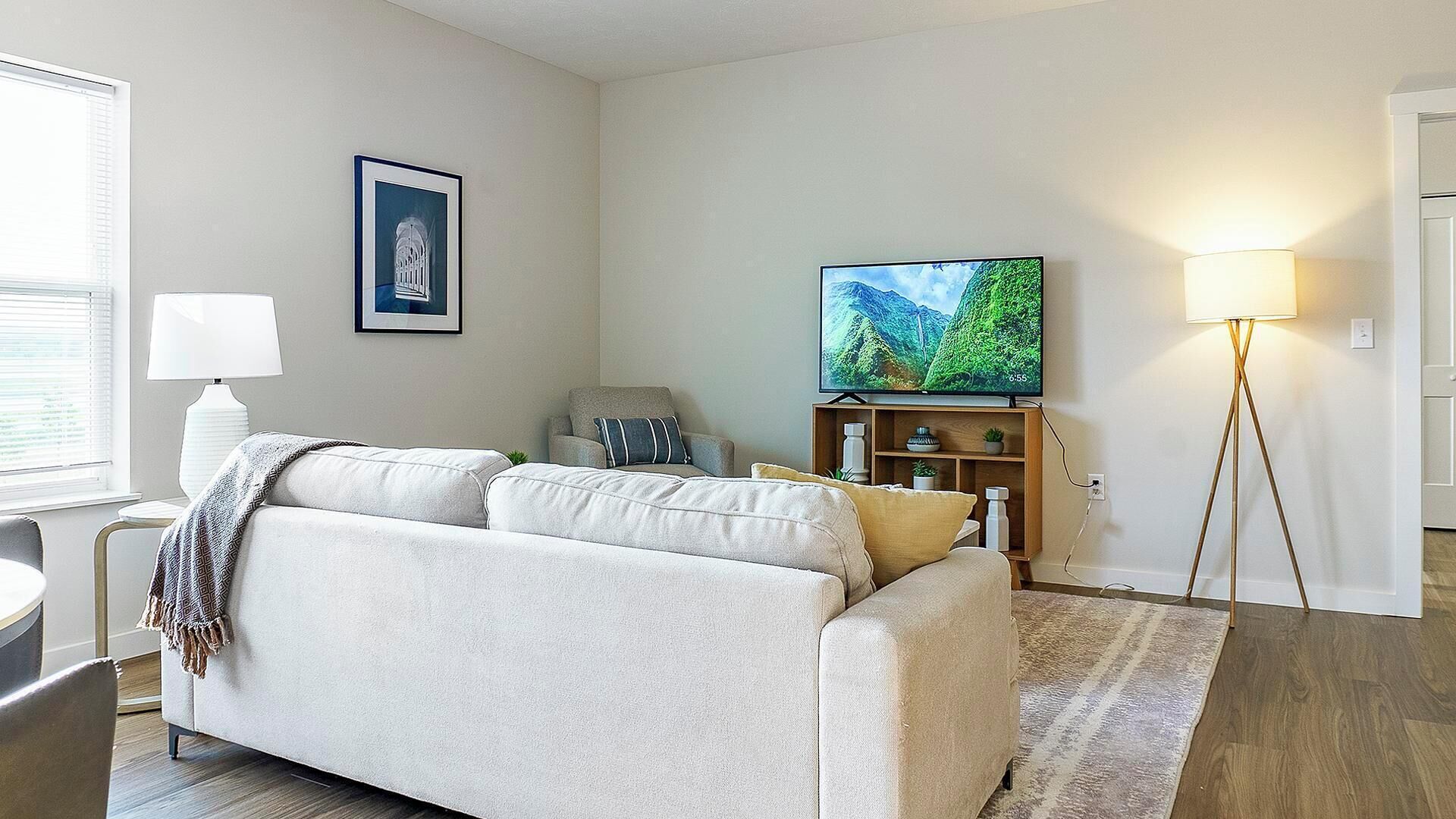 Ein Wohnzimmer mit einer Couch, einem Fernseher, einer Lampe und einem gerahmten Bild an der Wand.