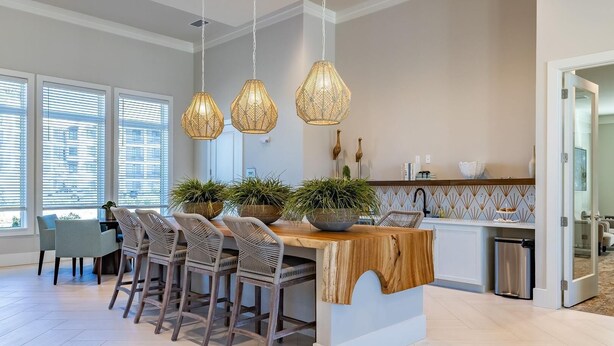 A modern kitchen with a central island, pendant lights, and a dining area with chairs.