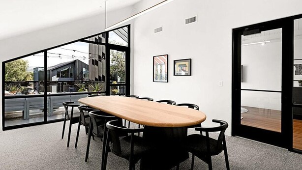 A modern conference room with a large table, black chairs, and large windows offering a view of buildings and greenery.