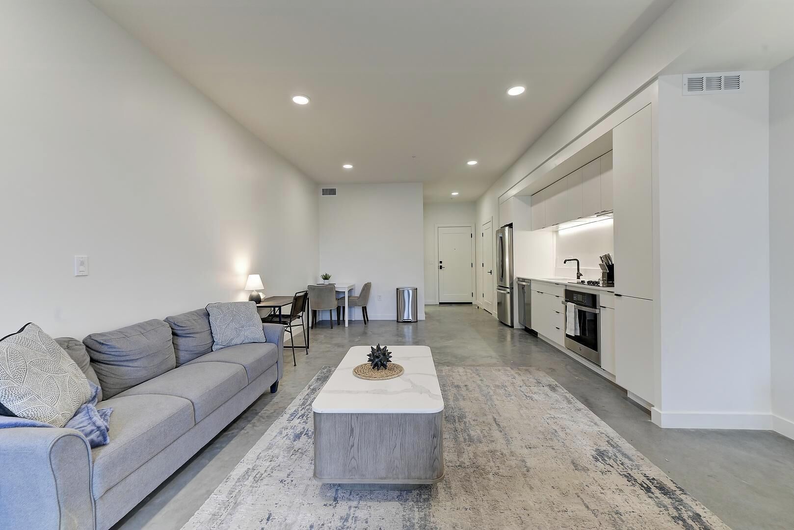 A modern living room with a grey sofa, a coffee table, and a dining area with chairs and a table.