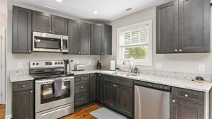 A modern kitchen with dark cabinets, stainless steel appliances, and a window providing natural light. - White Pine Sycamore by Avantstay Near Downtown (Asheville)