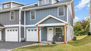 A two-story house with a garage, a covered porch with chairs, and a well-maintained lawn. - White Pine Sycamore by Avantstay Near Downtown (Asheville)