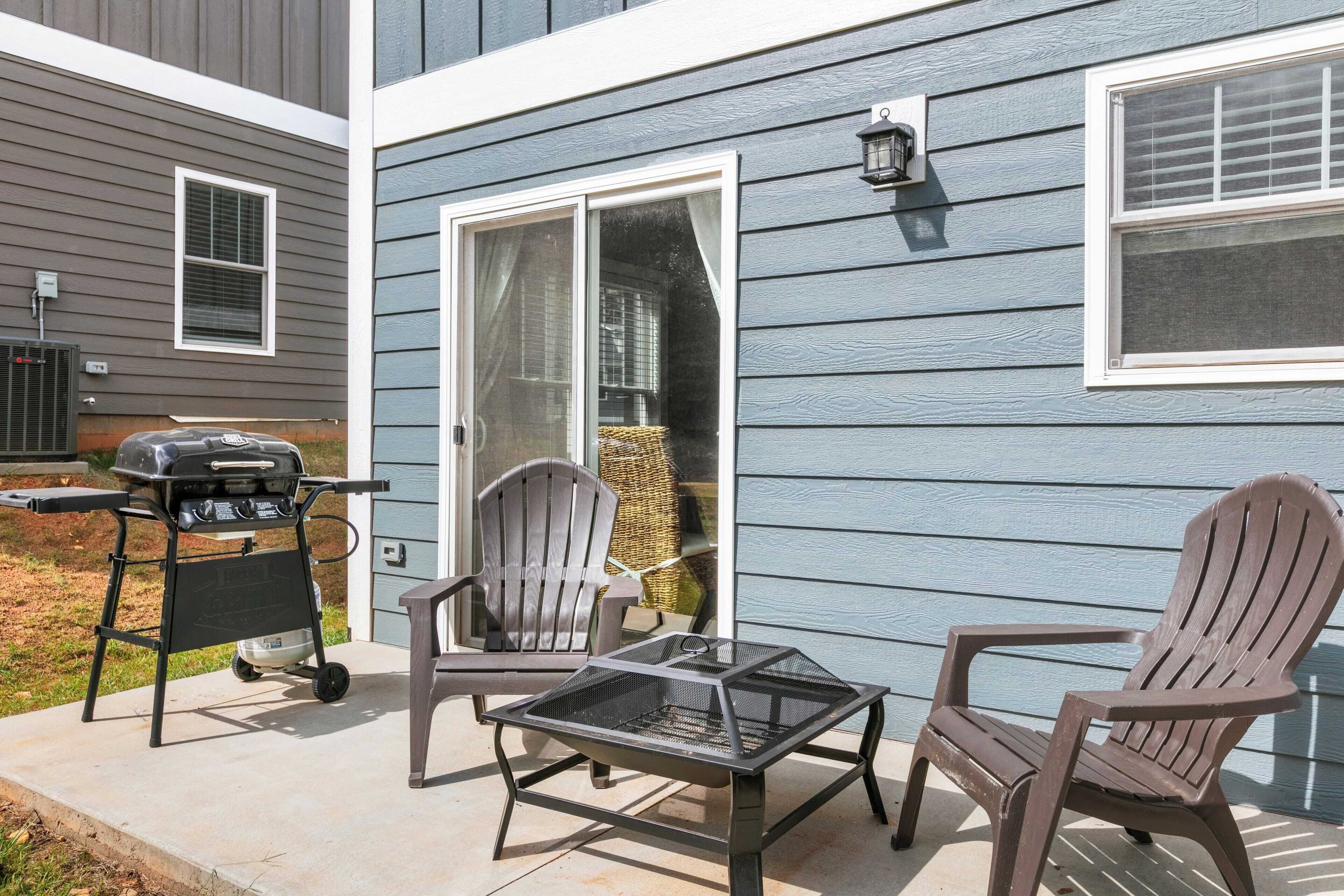 A patio with a grill, two Adirondack chairs, and a table.