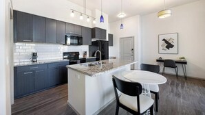 A modern kitchen with dark cabinets, a granite countertop, and a central island with a sink. - Landing | Stylish 1BD, Gym (Glendale)