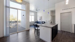 A modern kitchen with a central island, a dining area with a blue sofa, and a large sliding glass door leading to a balcony. - Landing | Stylish 1BD, Gym (Glendale)