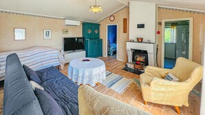 A cozy living room with a sofa, armchair, and a round table. There's a fireplace, a television, and a door leading to another room. - 1 bedroom beautiful home in Ljungskile (Ljungskile)