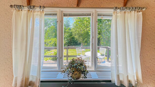 A window with white curtains, a potted plant on the sill, and a view of a garden outside. - 1 bedroom beautiful home in Ljungskile (Ljungskile)