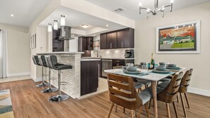 A modern kitchen with dark cabinets, a white island, and a dining area with a table and chairs.