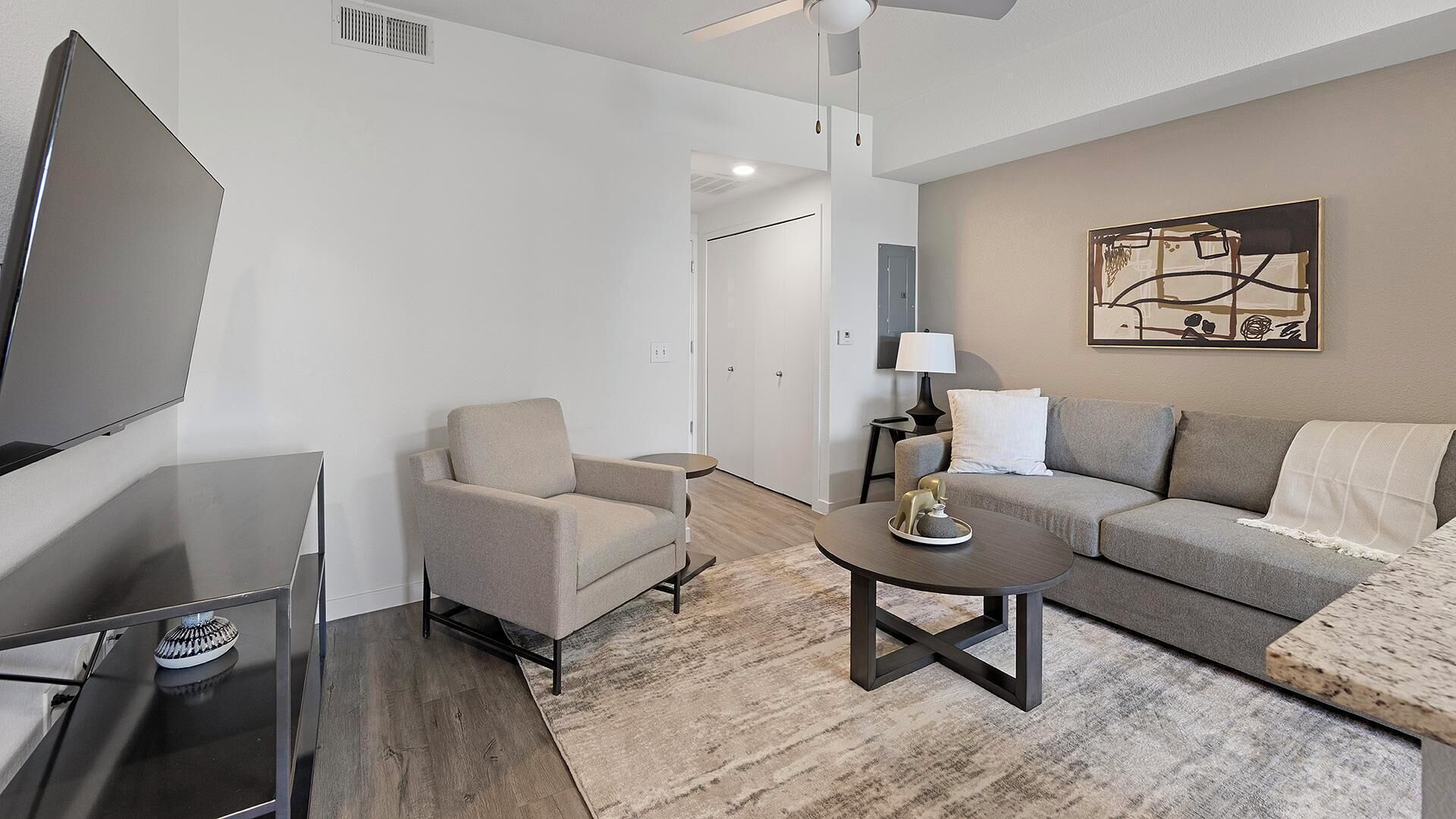 A modern living room with a flat-screen TV, a sofa, a chair, a coffee table, and a painting on the wall.