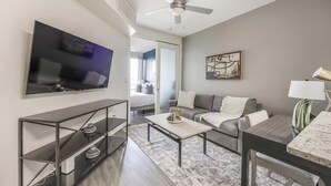 Une chambre d’hôtel moderne équipée d’une télévision à écran plat, d’un canapé, d’une table basse, d’un bureau avec une lampe et d’un tableau au mur.