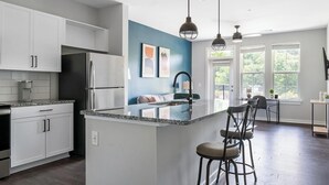 Una cocina moderna con armarios blancos, un refrigerador de acero inoxidable, una isla con encimera de granito y una pared de acento azul.