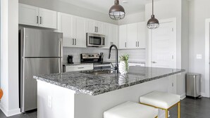 A modern kitchen with white cabinets, stainless steel appliances, granite countertops, and pendant lighting.