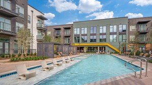 Een modern appartementencomplex met een zwembad, ligbedden en een gele glijbaan.