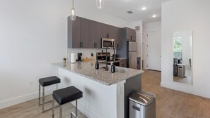 Une cuisine moderne avec des meubles gris, des appareils en acier inoxydable, un comptoir en granit et deux tabourets de bar noirs.