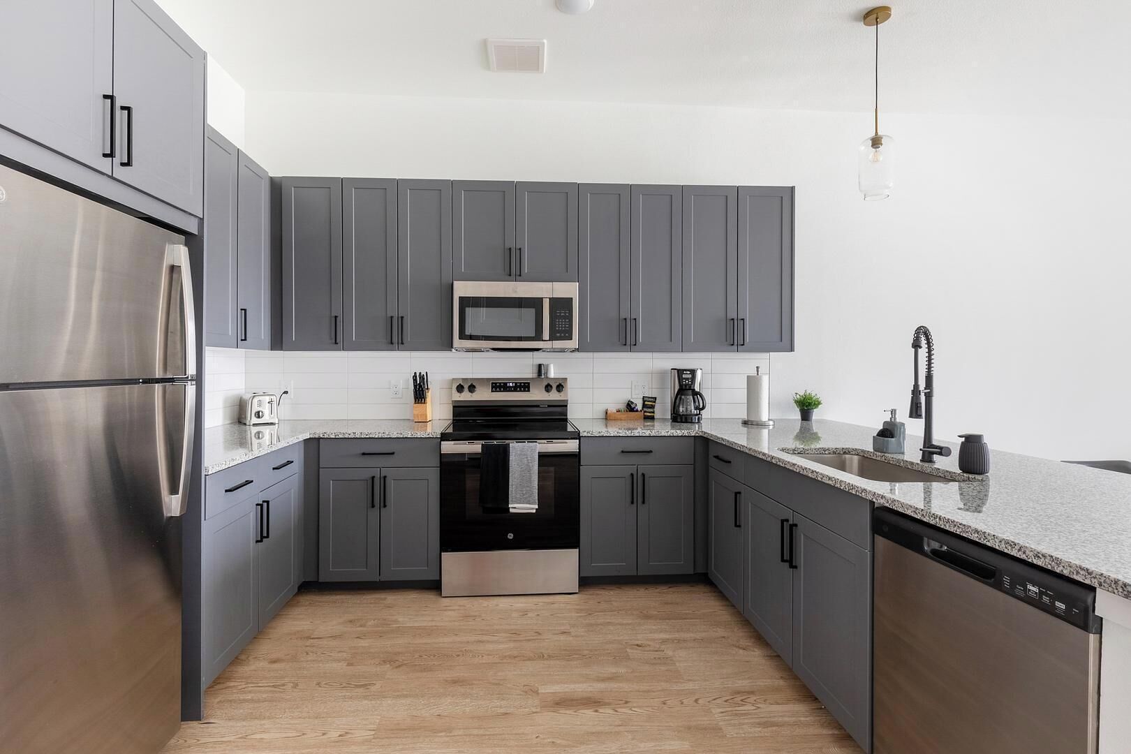 Eine moderne Küche mit grauen Schränken, Edelstahlgeräten, einer Arbeitsplatte aus Granit und Holzboden.