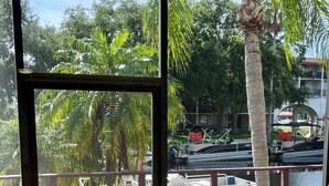 Blick von einem Balkon mit Holzterrasse auf einen Yachthafen mit Booten und Palmen.