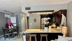Eine moderne Küche mit dunklen Schränken, einer weißen Arbeitsplatte und einem eingebauten Backofen. Es gibt einen Essbereich mit Tisch und Stühlen sowie ein Wohnzimmer mit Sofa und Couchtisch.