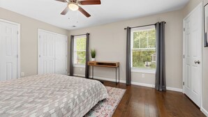 Un dormitorio con cama, ventilador de techo, ventana con persianas, mesita de noche y puerta.