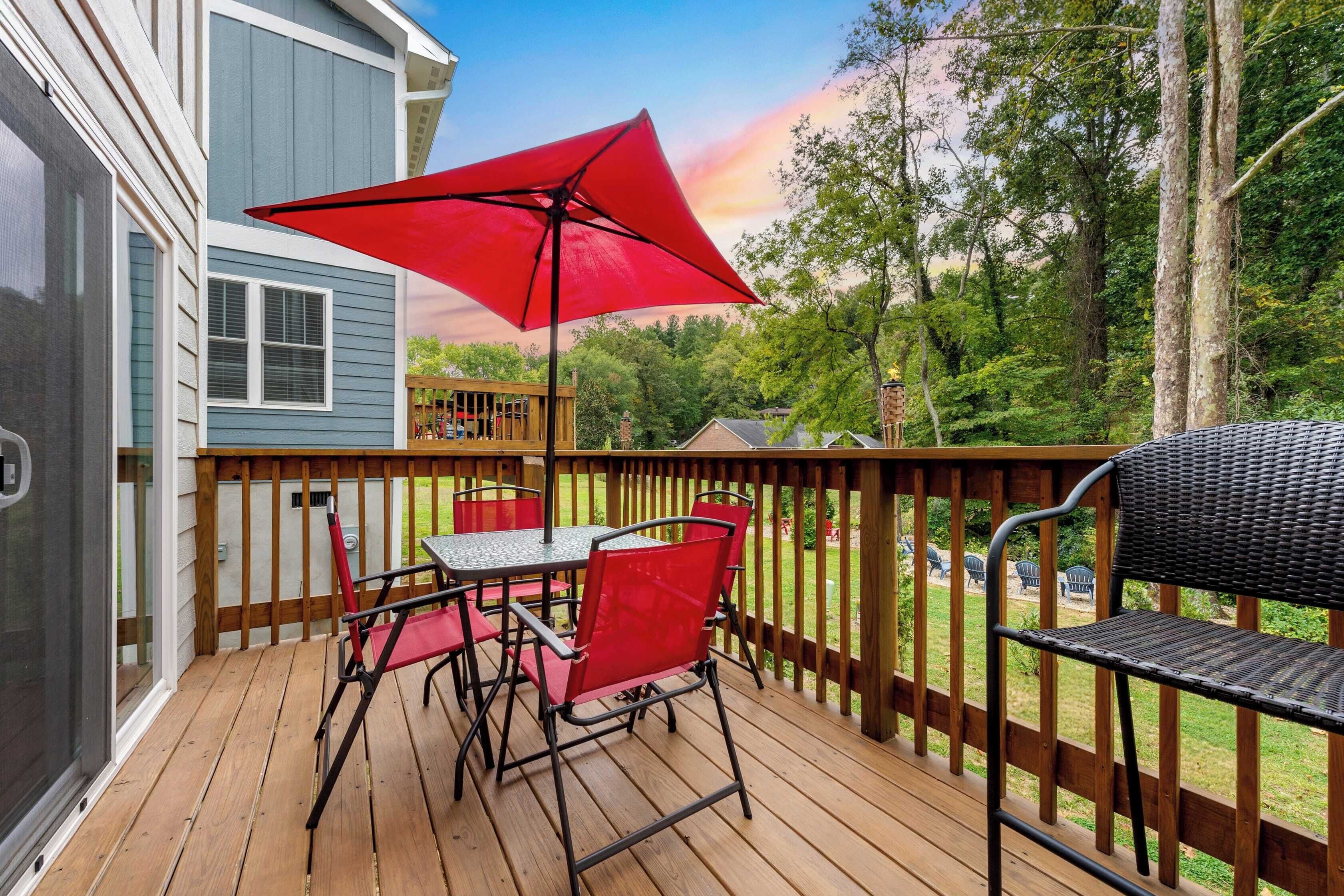 A wooden deck with a table and chairs, a red umbrella, and a grill.