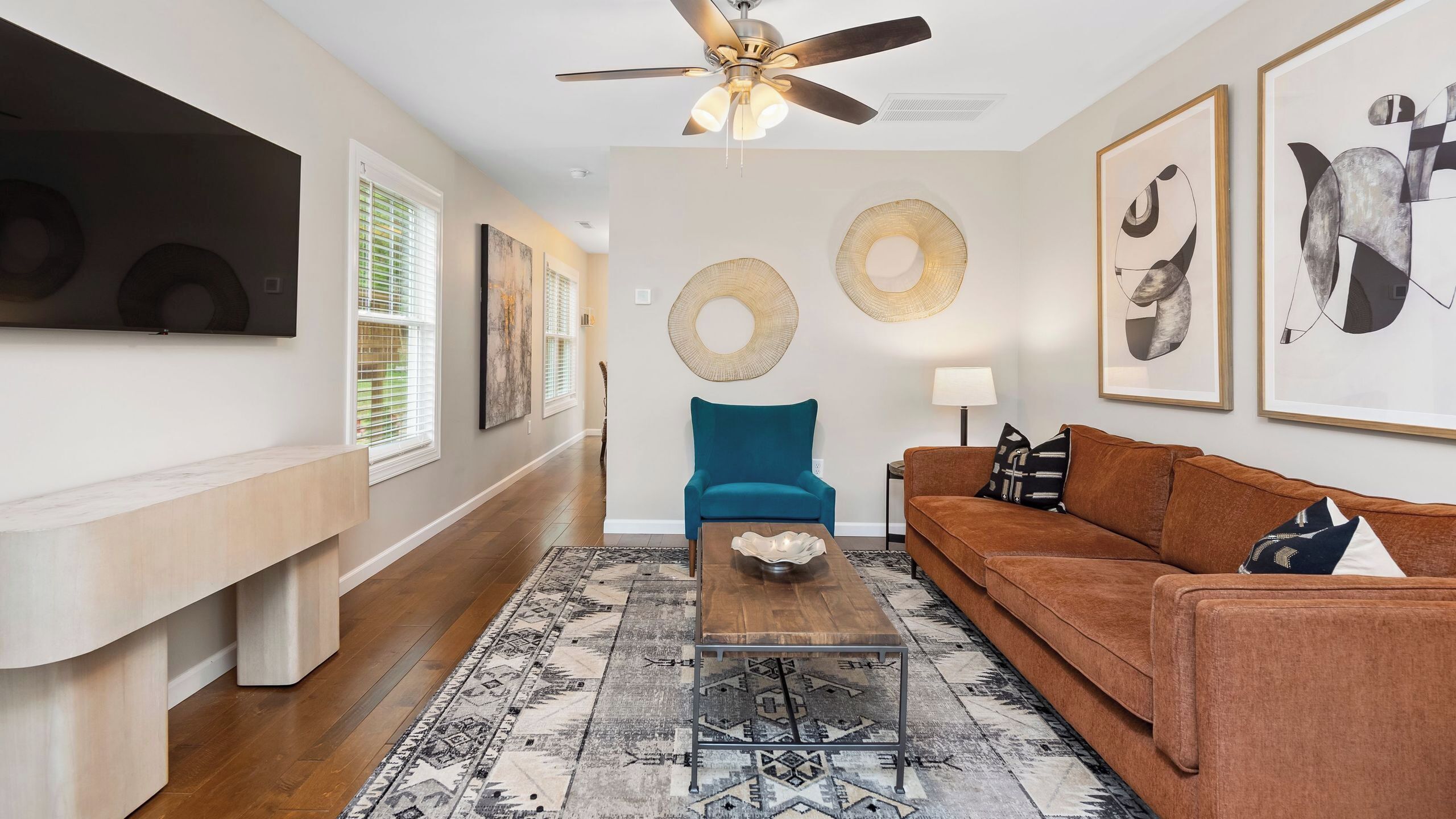 A living room with a ceiling fan, a blue armchair, a brown sofa, a coffee table, and a patterned rug.