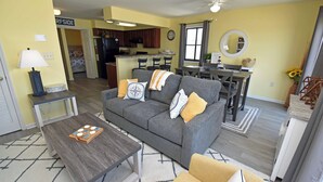 A living room with a gray sofa, a coffee table, and a dining area with a table and chairs. - Sandfiddler 301 - Oceanfront Condo in Surfside Beach (Surfside Beach)