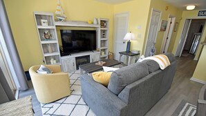 A living room with a grey sofa, a yellow armchair, a TV, and a fireplace. - Sandfiddler 301 - Oceanfront Condo in Surfside Beach (Surfside Beach)