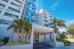 A modern hotel entrance with a geometric facade, palm trees, and a clear sky.