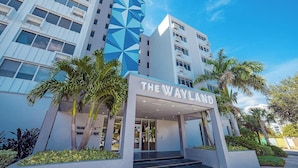 A modern hotel entrance with a geometric facade, palm trees, and a clear sky. - Landing | Stylish Studio, Pool, Clubhouse (St. Petersburg)