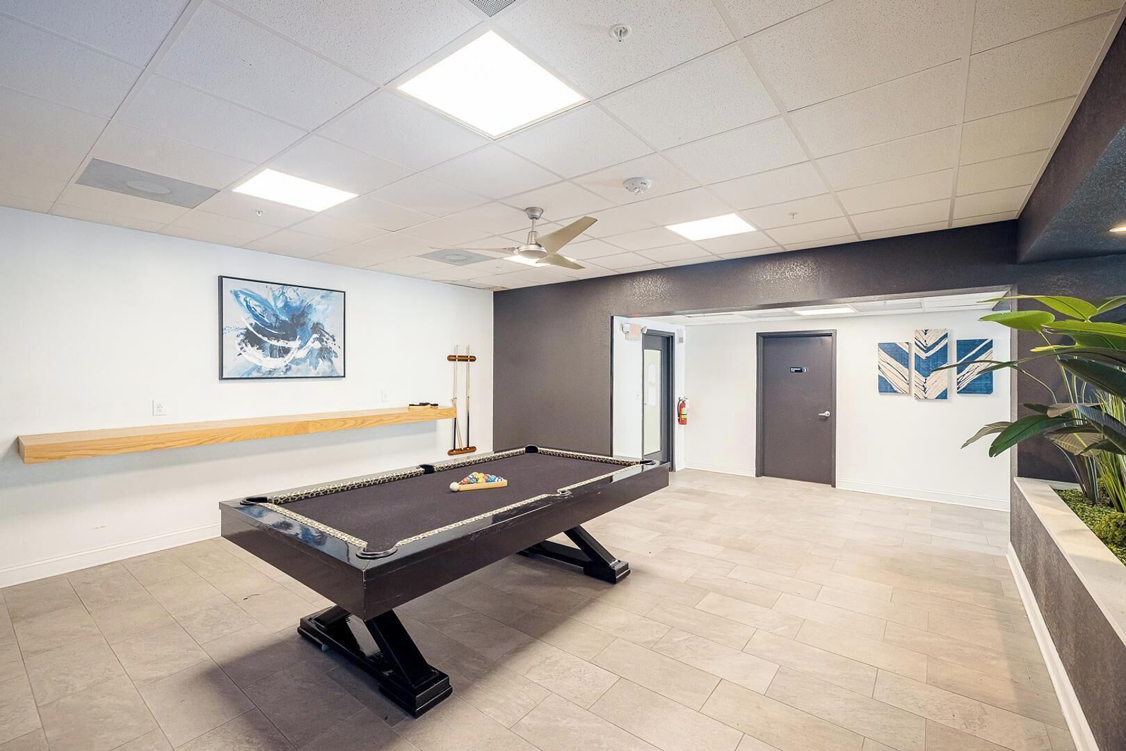 A pool table in a room with a ceiling fan, a fire extinguisher, and a door.