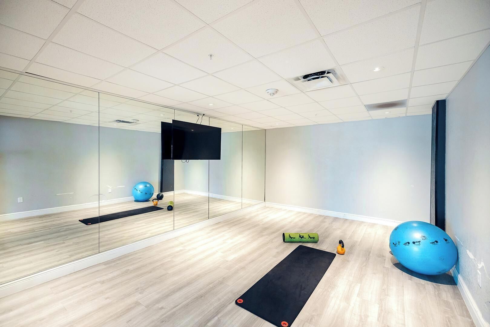 Un gimnasio moderno con un espejo grande, pelotas de ejercicios, una colchoneta de yoga y una pantalla de televisión.