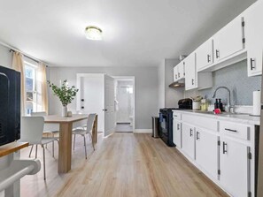 A modern kitchen with white cabinets, a wooden dining table, and a view into the adjacent bathroom.