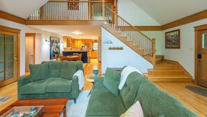 A spacious living area with a high ceiling, a wooden staircase, and a kitchen in the background. - The Wander Inn | Pet-friendly, Screened Porch, Game Room & Walking Distance to Town! (Black Mountain)
