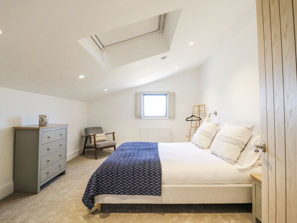 A bedroom with a bed, a dresser, a chair, a window, and a skylight. - Number 2 The Barn House (Aylesbury)