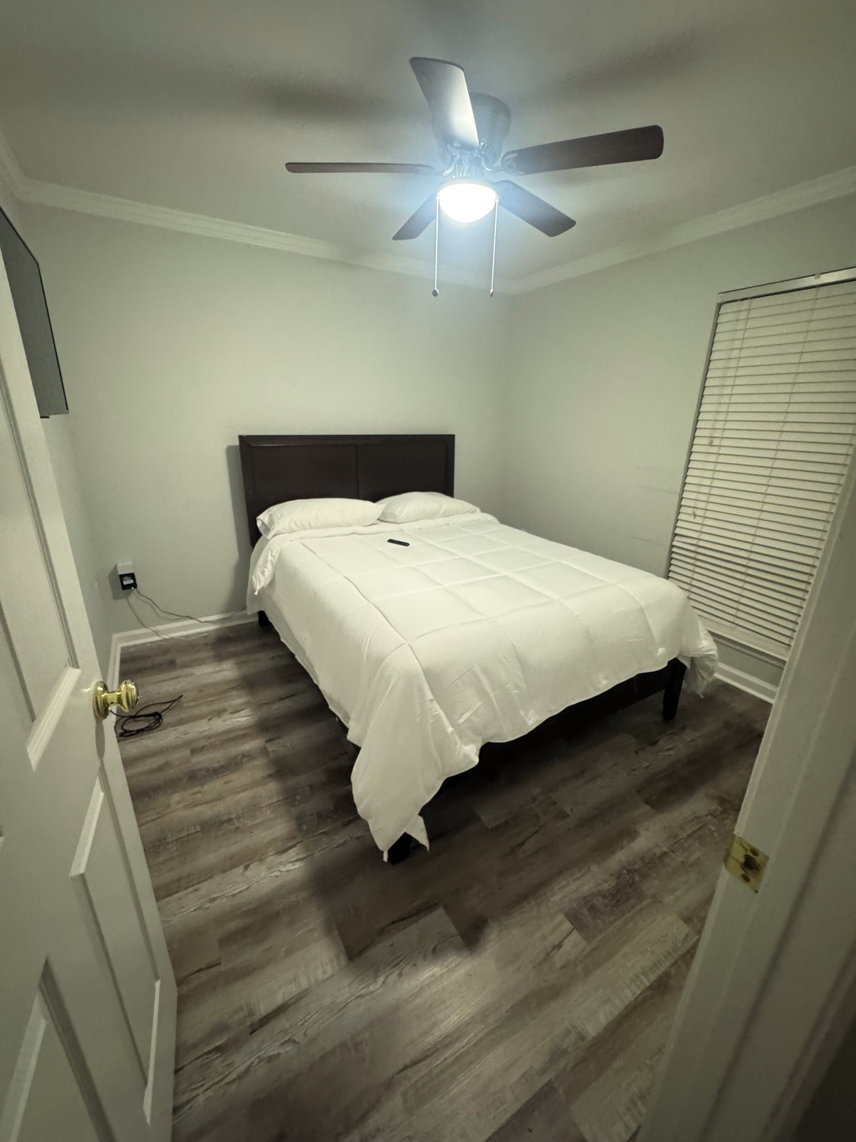 A bedroom with a bed, a ceiling fan, and a door.
