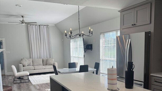 A modern kitchen with a central island, a dining area with a sofa and chairs, and a living room with a couch and a ceiling fan. - Charming 3-bedroom house with AC in Prairieville (Prairieville)